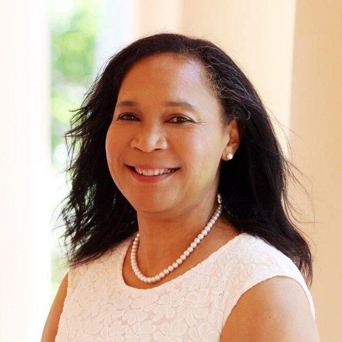 A woman with long black hair wearing pearls.