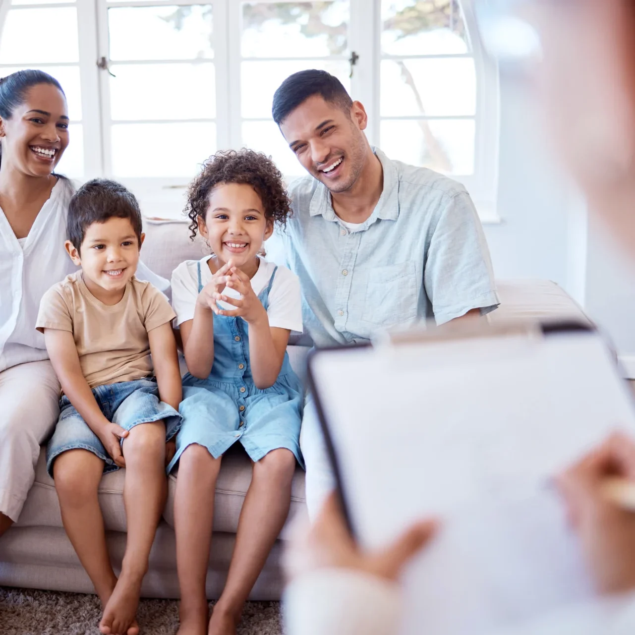 A family sitting on the couch looking at a woman.