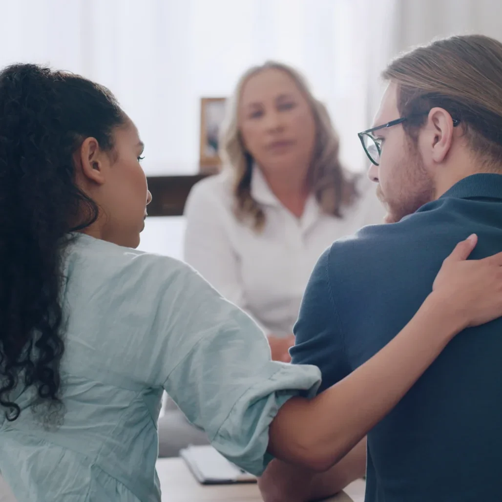 A woman and man hugging in front of another person.