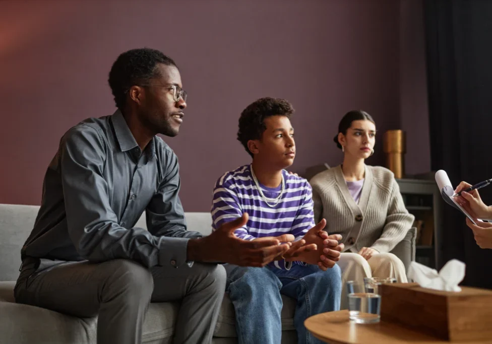 Three people sitting on a couch in front of a wall.