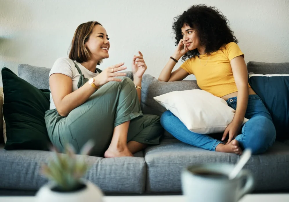 Two women sitting on a couch talking to each other.