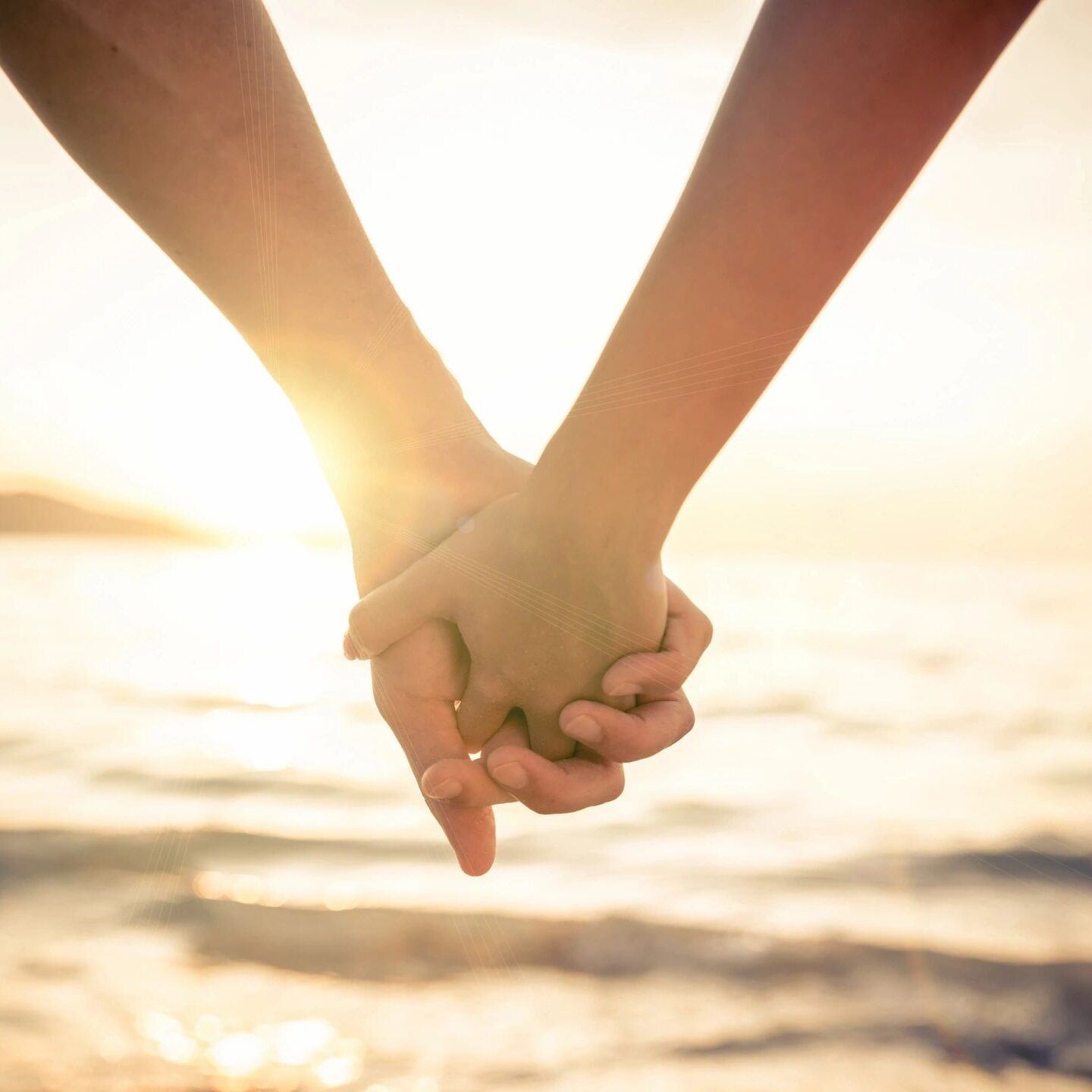 Two people holding hands in front of the ocean.